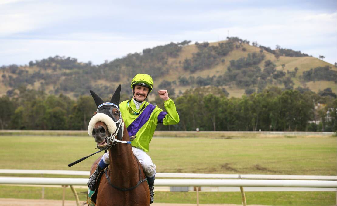 Jockey celebrating a win with a raised fist against a hills backdrop